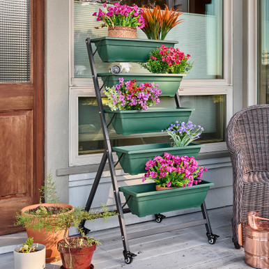 Green vertical planter with five blooming garden boxes on wheels outside a home window