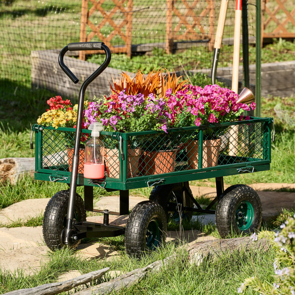 Green utility garden cart filled with potted flowers on a stone path