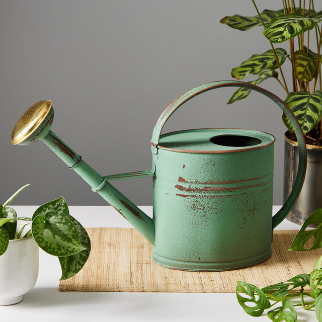 Vintage-style copper watering can on white table next to potted plants